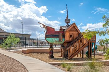 A playground with a wooden pirate ship structure and a green slide.